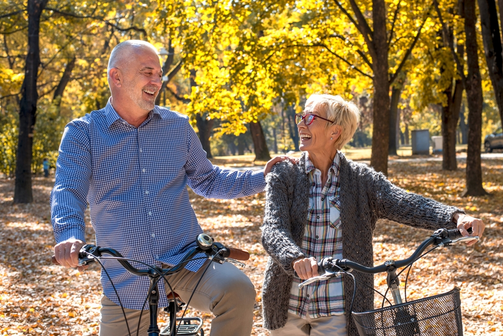 A happy elderly couple riding a bicycle in the park in the autumn